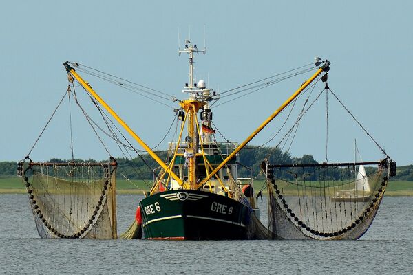 Ein Fischerboot in Küstennähe mit Schleppnetzen rechts und links.