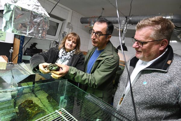Zwei Männer und eine Frau stehen in den Räumen des Stuttgarter Tierheims vor einem Terrarium. Cem Özdemir hält eine Schildkröte in der Hand.