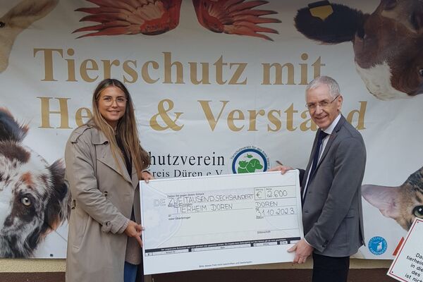 Eine Frau und ein Mann halten einen großen Scheck in den Händen. Hinten ein Plakat des Tierschutzvereins.