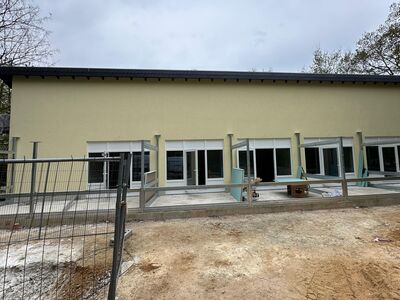 Ein hell angestrichenes, einstöckiges Gebäude mit fünf mal zwei großen Fenstern und einer Tür.