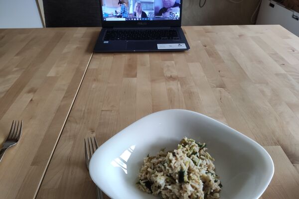 Ein Laptop steht auf einem Esstisch, davor ein Teller Reispfanne mit Gemüse.
