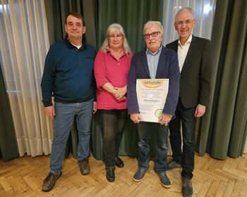 Eine Frau und drei Männer, ein Mann hält eine Ehrenurkunde den Händen.