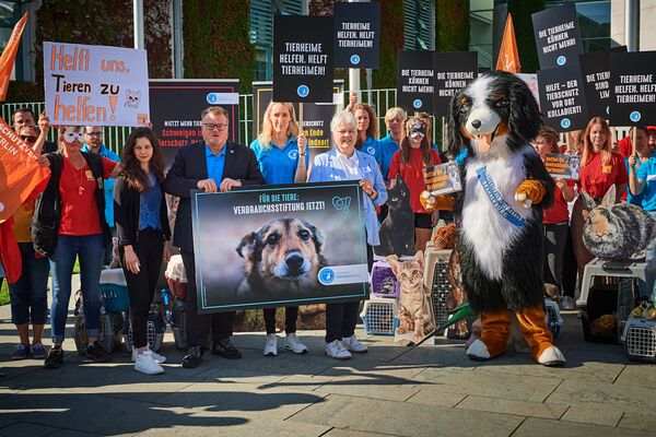 Eine Personengruppe mit Plakaten und eine Person im Hundekostüm fordern mehr Unterstützung für Tierheime.
