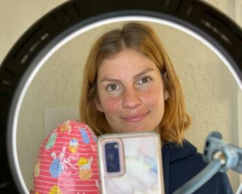 Eine Mitarbeiterin mit Handy und Lampe, die ein bunt verpacktes Schokoladenei in der Hand hält