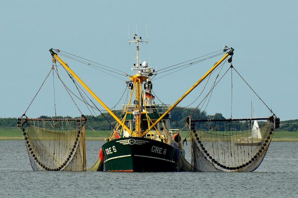 Ein Fischerboot in Küstennähe mit Schleppnetzen rechts und links.